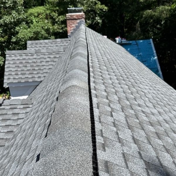 Gray shingle roof, close-up view of a roof peak with a brick chimney in the background.