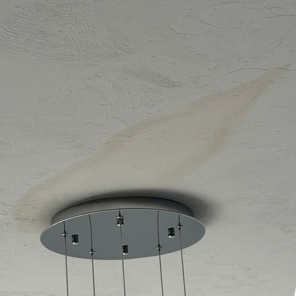 A large, discolored water stain on a white textured ceiling surrounding the mounting plate of a modern light fixture.