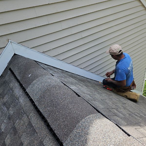 Roofer installing flashing on a gray shingle roof next to gray siding.