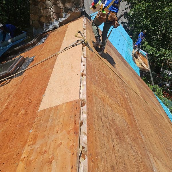 Construction workers on a roof, installing wooden panels. Brown wood, blue tarp, sunny outdoors.