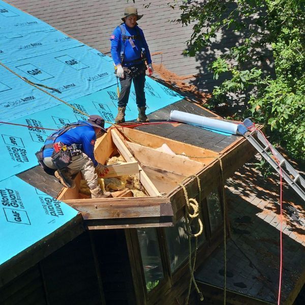 Two roofers on a roof repairing a wooden structure, blue safety lines.