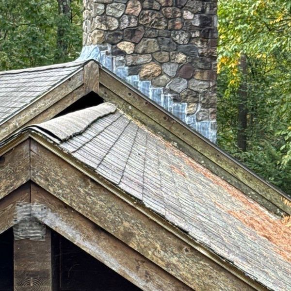 Stone chimney rising from a wooden roof with weathered shingles.