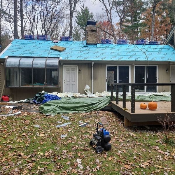 House with blue roof under construction, deck, pumpkins, trees, and fallen leaves.