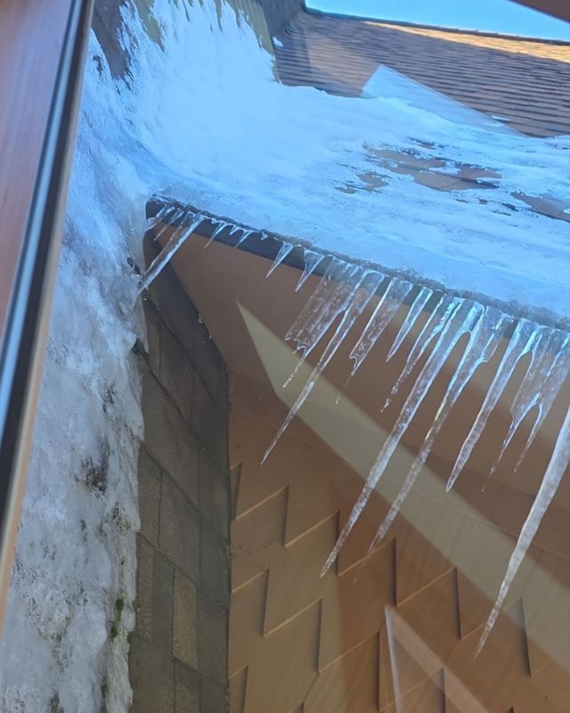 Icicles hanging from a roof with ice and snow. Brown roof with a blue sky visible.