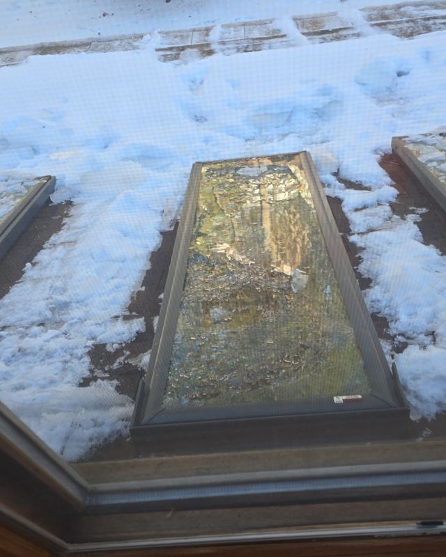 Skylight on a snow-covered roof; rectangular, with dark frame, snow surrounds it and partially obscures glass.