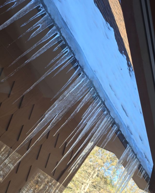 Icicles hanging from a brown roof under a blue sky.