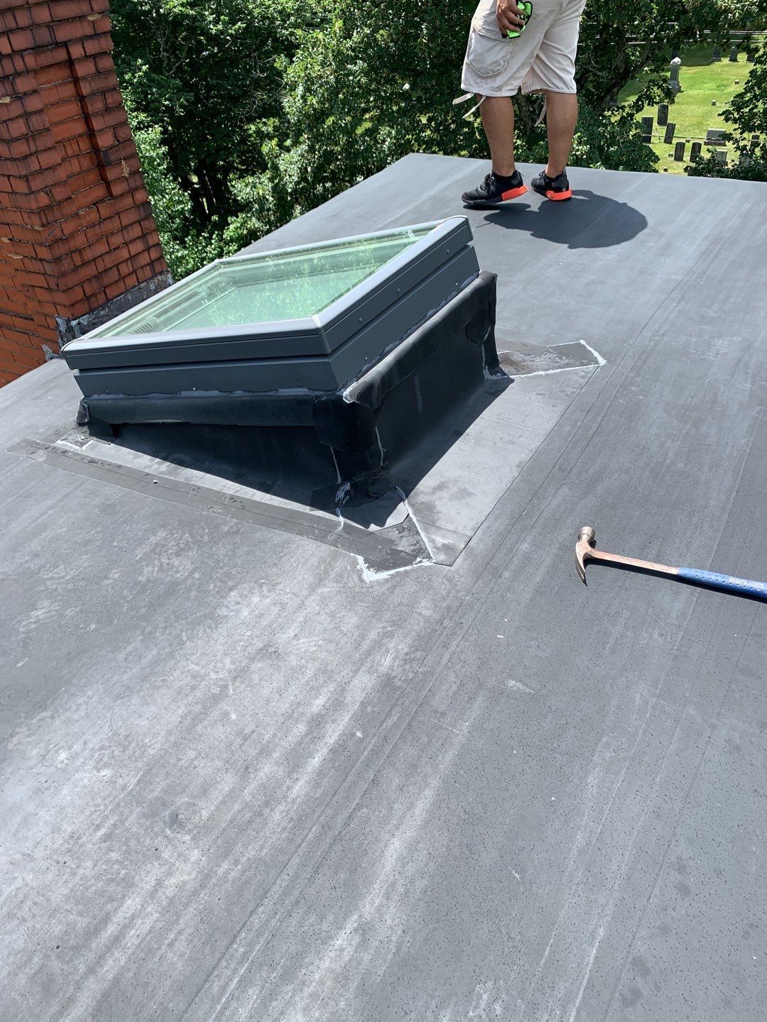 Black flat roof with a skylight, a person standing nearby, and a hammer.