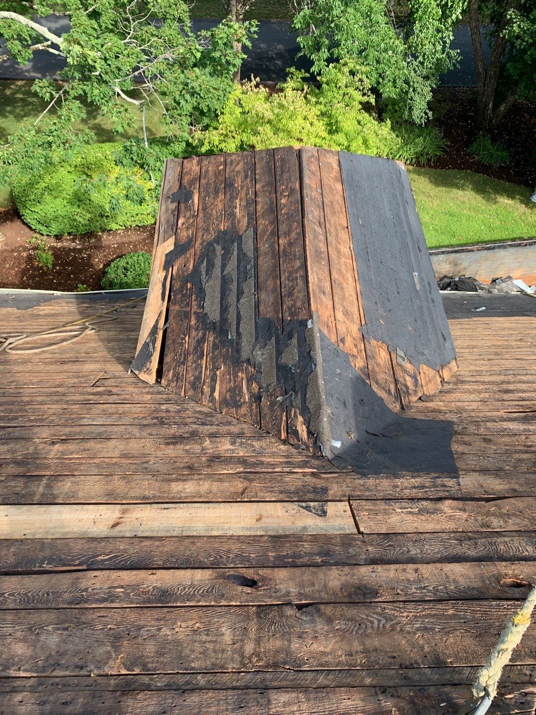 A roof repair in progress showing exposed wood decking and a partially shingled, raised roof vent structure.