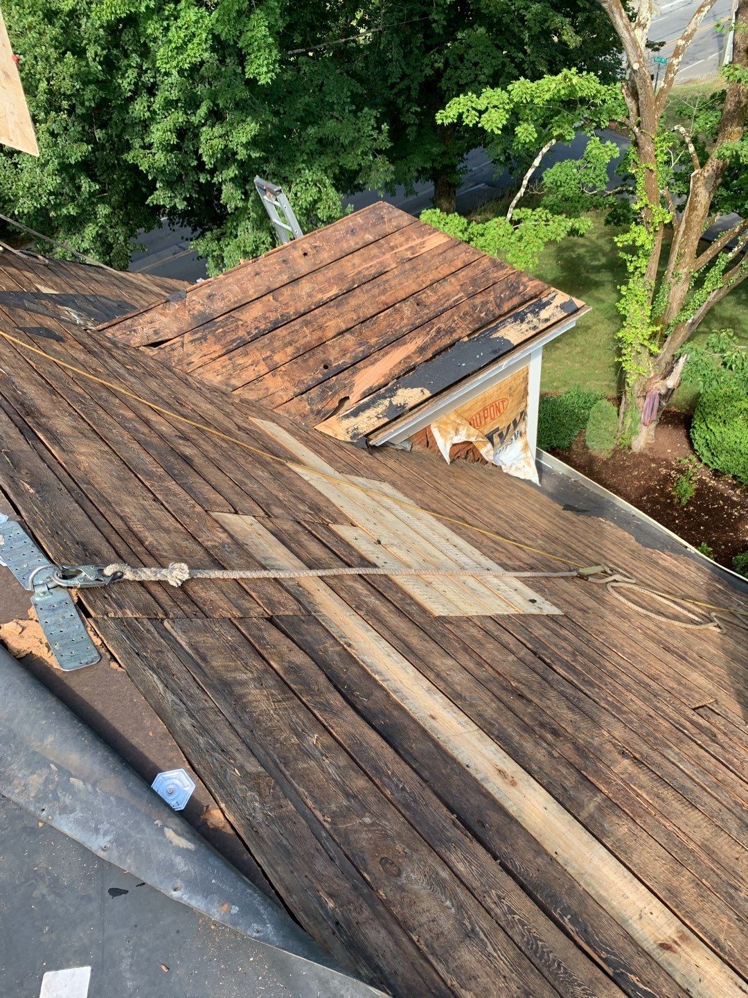 Damaged roof with exposed wooden boards; debris and surrounding trees in view.