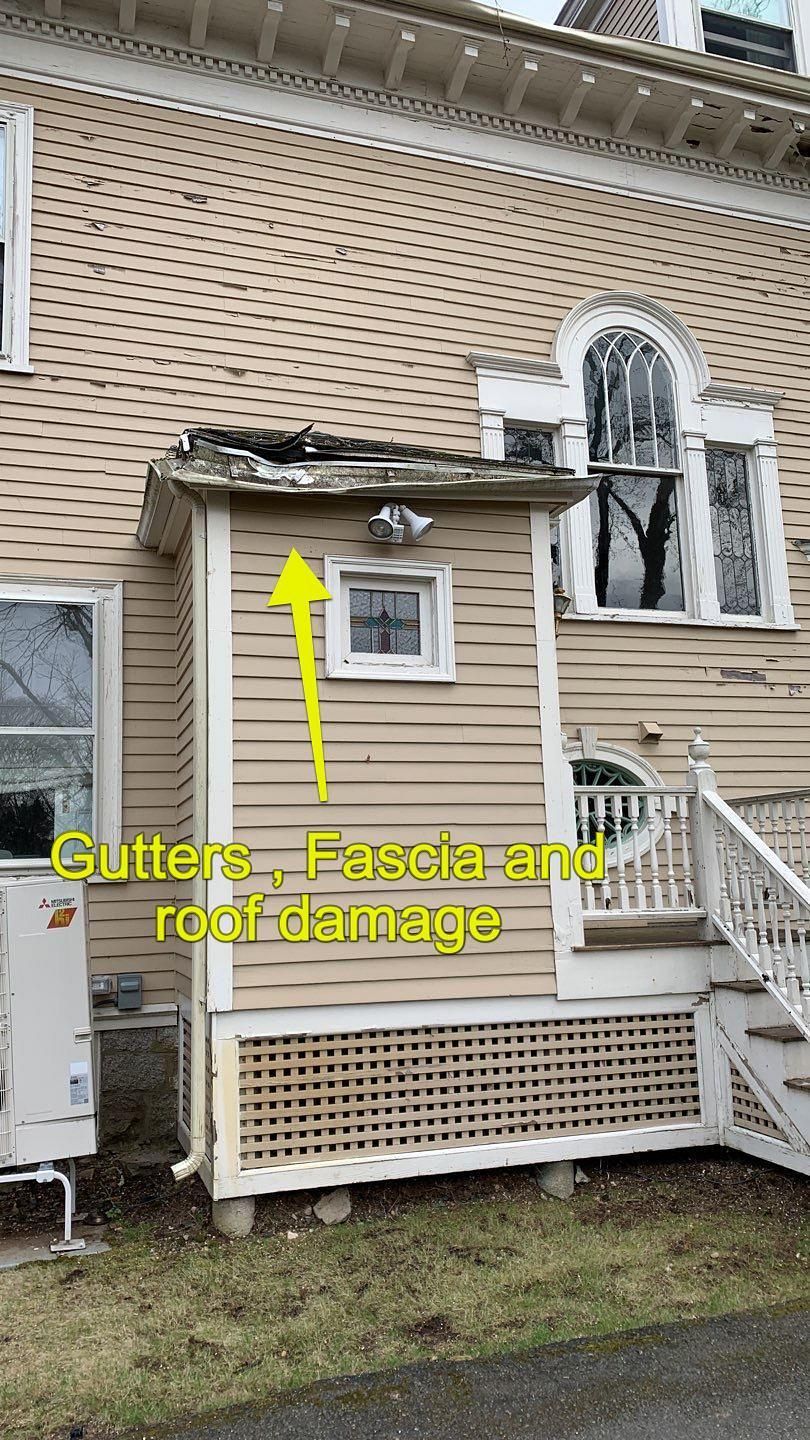 Tan house with a damaged roof, fascia, and gutter on a small side extension, highlighted by a yellow arrow.