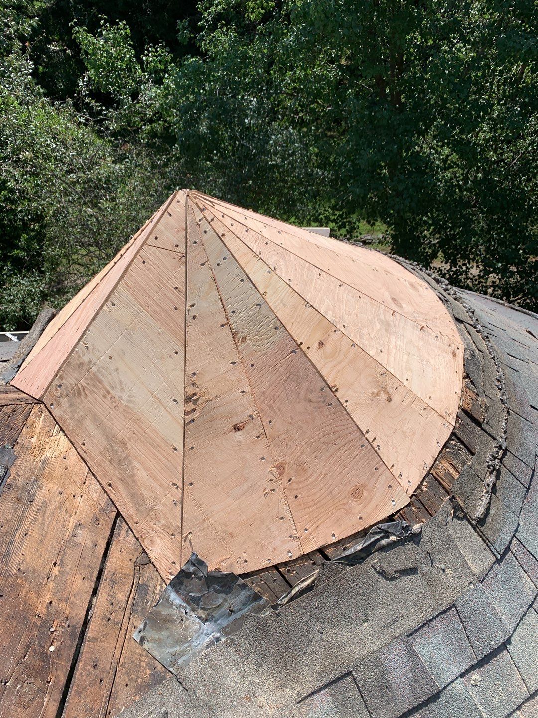 Wooden roof cone repair on a shingled roof, trees in the background.