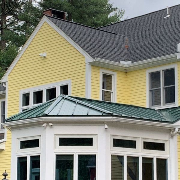 Yellow house with white trim, green roof, and multiple windows.
