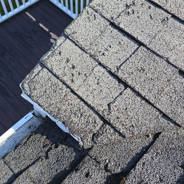 Close-up of weathered asphalt shingles on a roof corner, showing wear and tear, and a white gutter.