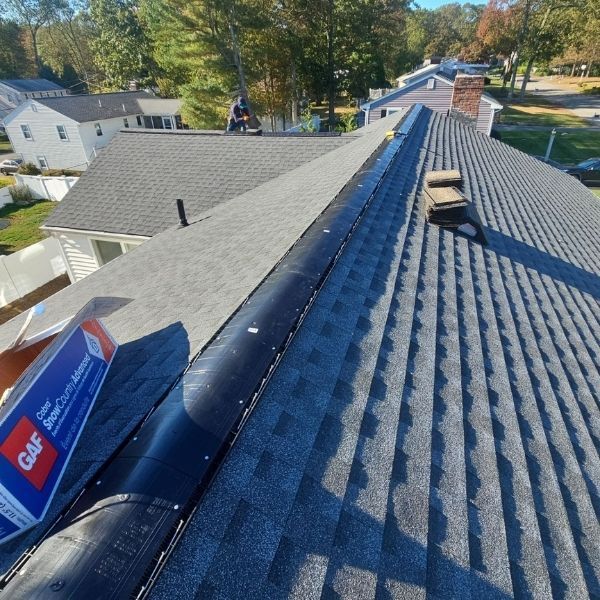 A roof under construction with gray shingles and black flashing. A package of shingles is visible.