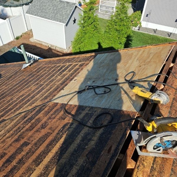Roof with exposed wood, tools, and a shadow, viewed from above.