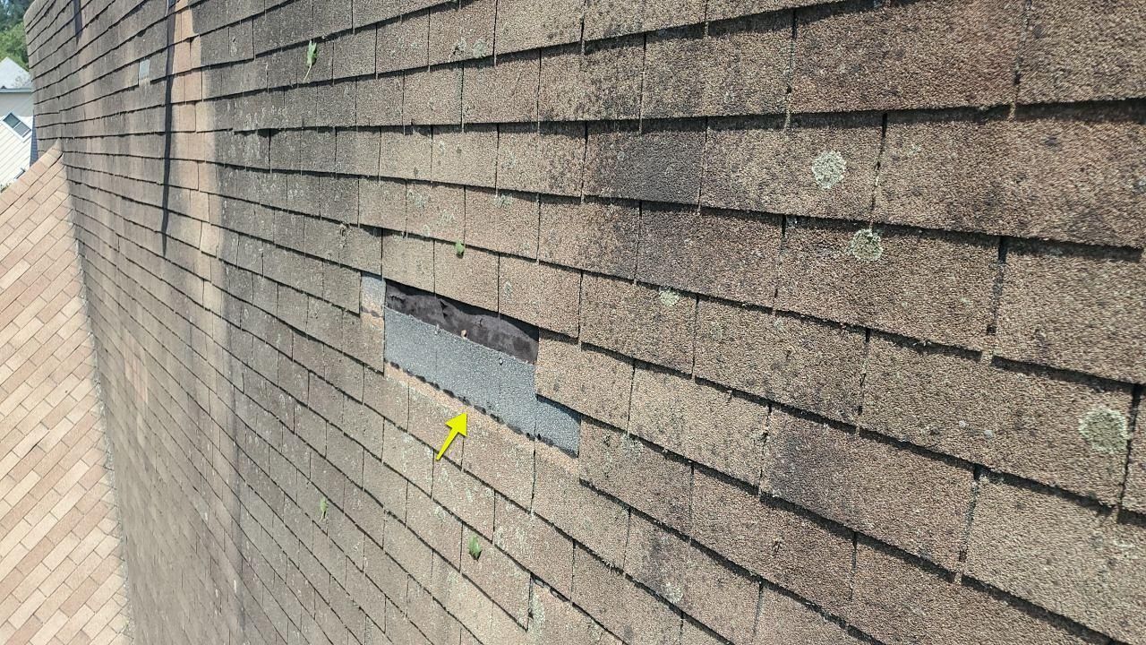 View of a brown asphalt shingle roof with missing shingles indicated by a yellow arrow.