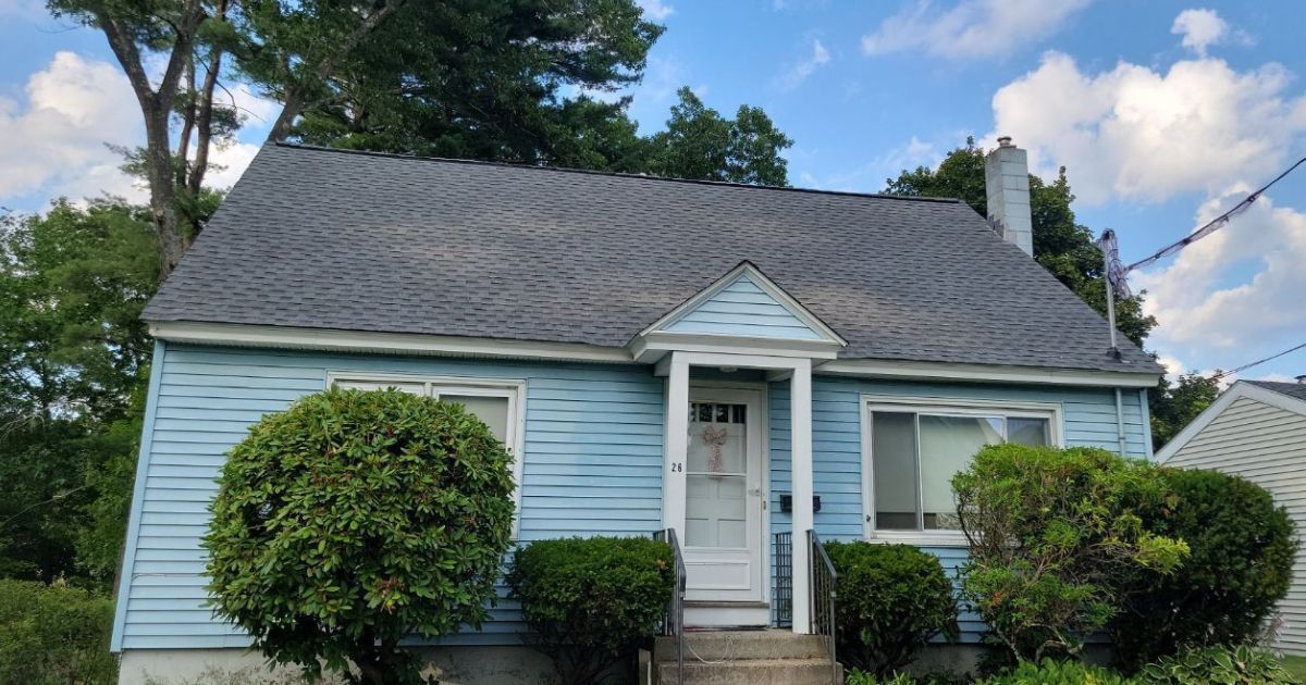 Blue house with dark roof and white trim; bushes in front.