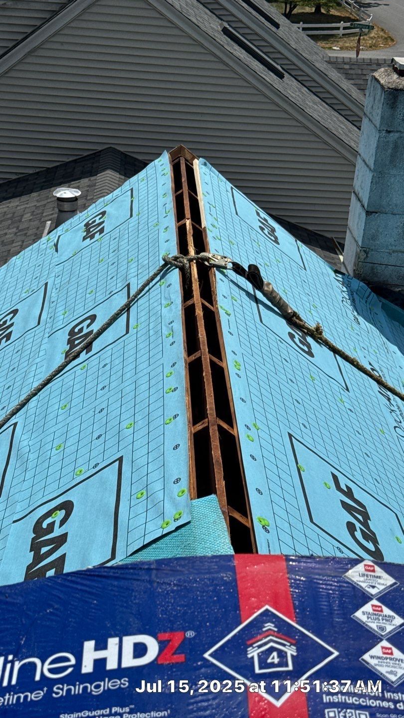 A roof ridge under construction with blue GAF underlayment and a visible gap for roof ventilation.