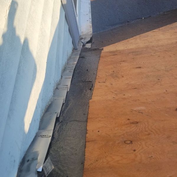 A roof transition showing metal step flashing tucked under white siding next to a layer of black roofing felt and plywood.