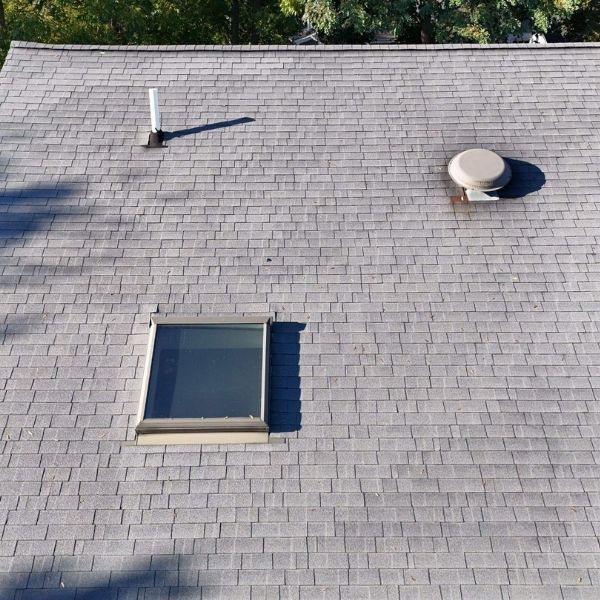 A gray shingled roof featuring a rectangular skylight, a white vent pipe, and a round roof vent.