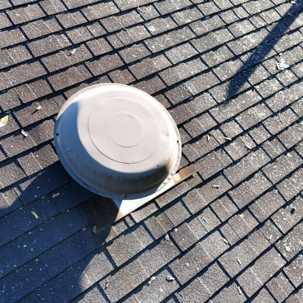 A circular, grey metal attic roof vent installed on a shingled residential roof.