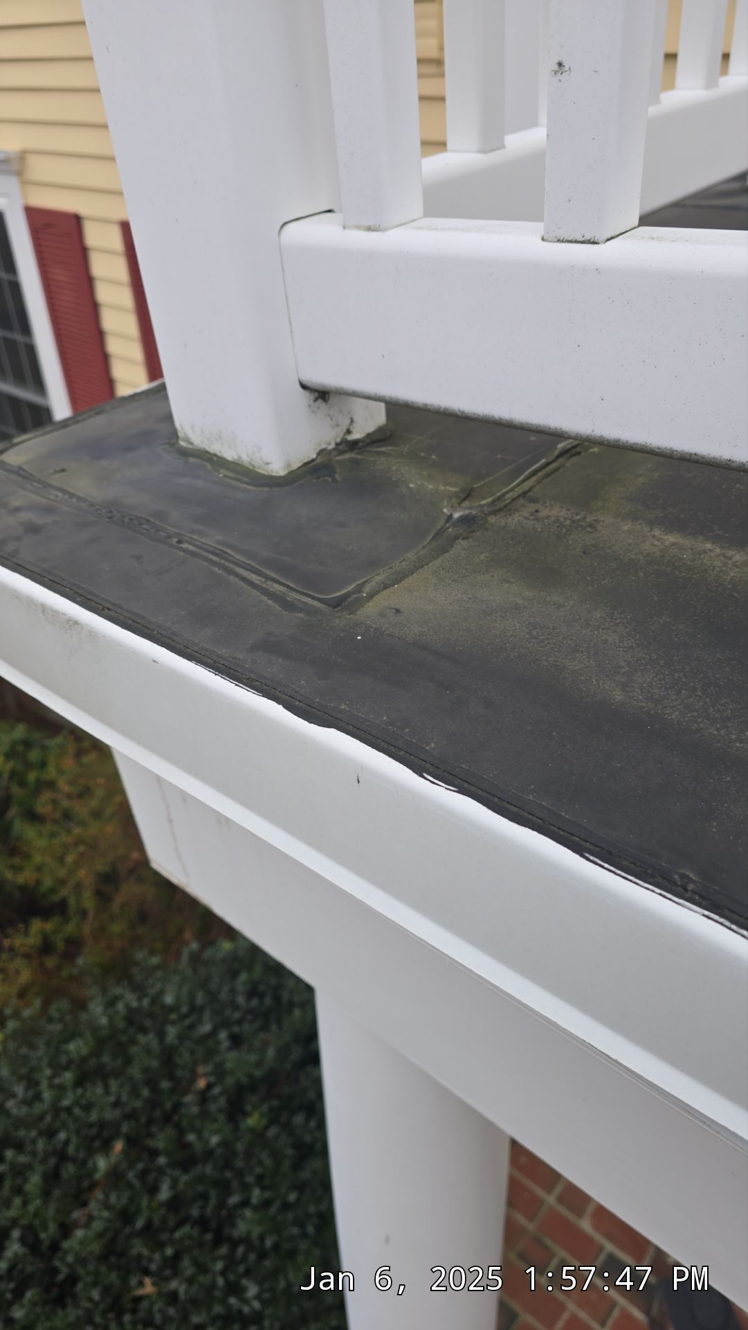 Close-up of a white railing post on a porch, black roofing material, and a white gutter.