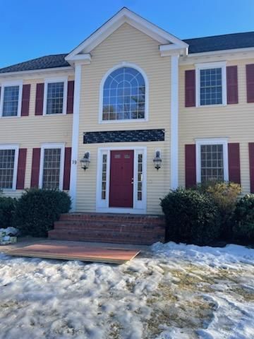 Yellow house with red shutters and door; front steps covered in snow.