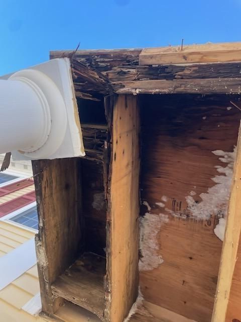 Damaged roof structure with vent, showing rotted wood, discoloration, and snow.