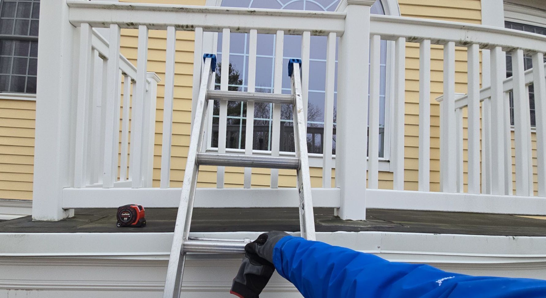 Person with gloved hand near ladder on porch, house in background.