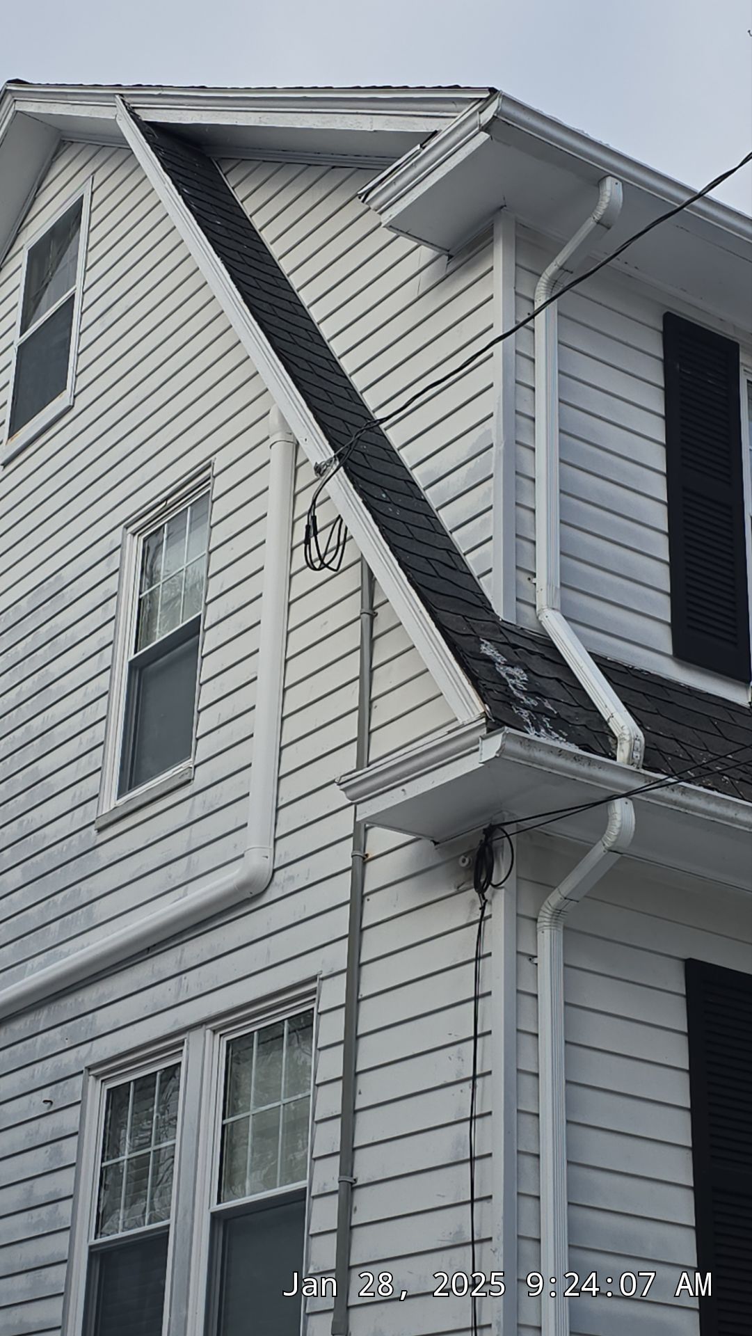 White house exterior with dark strip running diagonally. White trim, black shutters, and gutters visible.