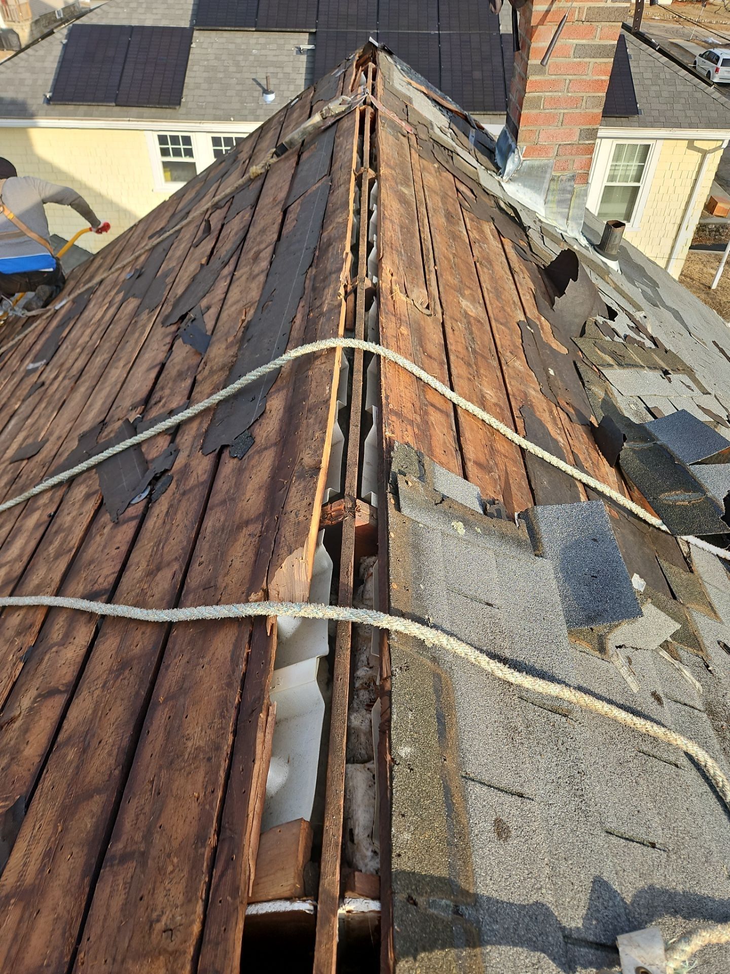 Rooftop undergoing repair, revealing wood underlayment and debris. Two safety ropes span the apex.