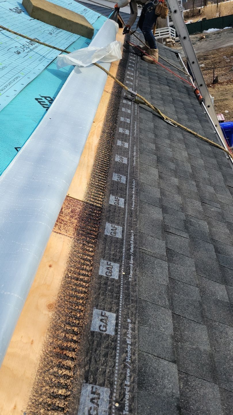 Roofer installs shingles on a house roof. Blue insulation and wood beams visible.