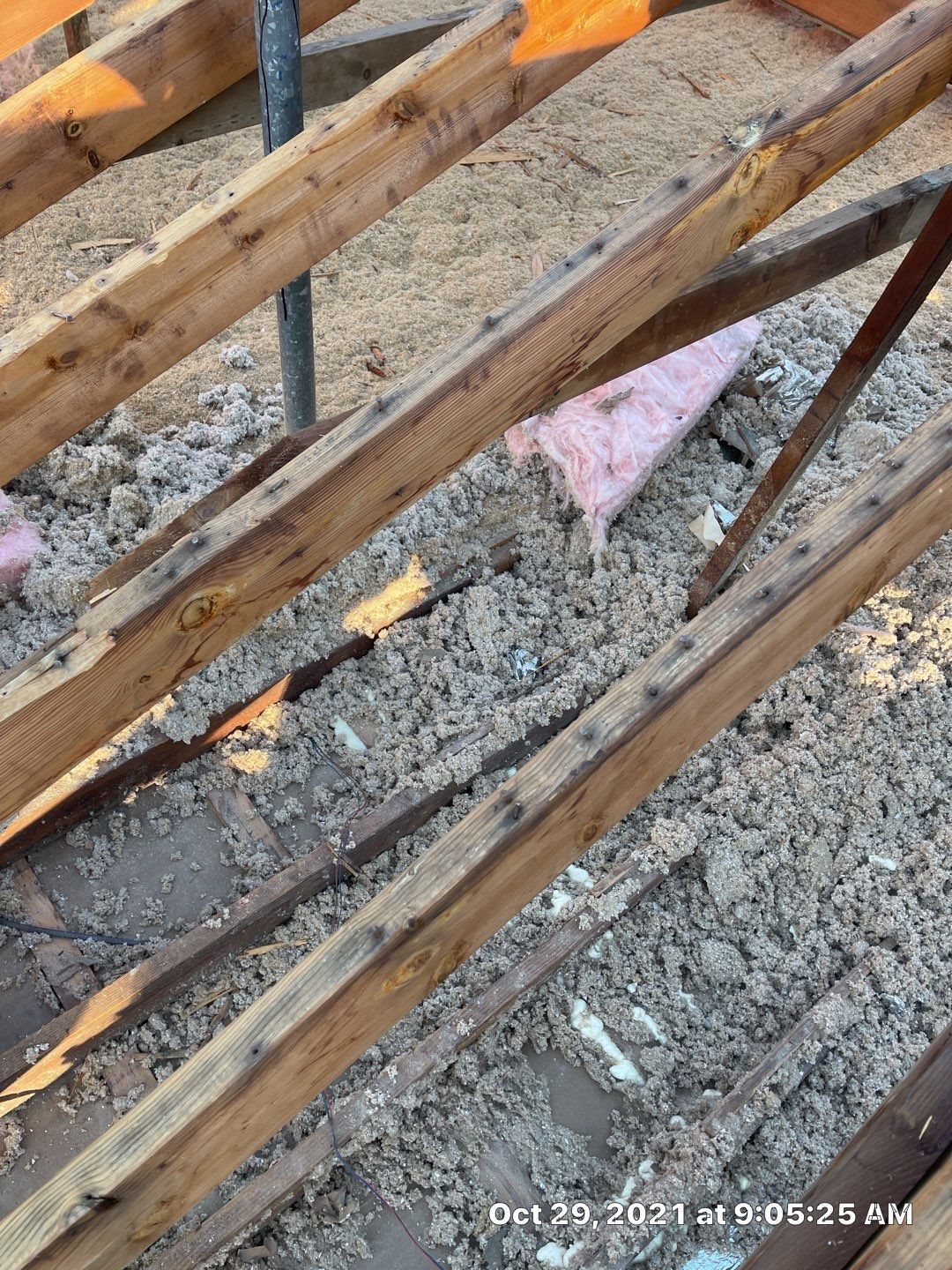 View of a partially insulated attic with wooden beams. Beige insulation is scattered.