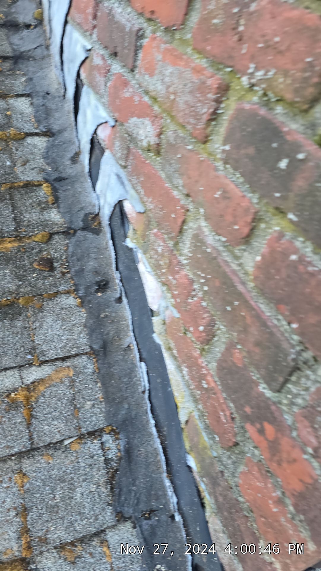 Brick chimney flashing with asphalt shingles. The flashing is weathered and has some separation.