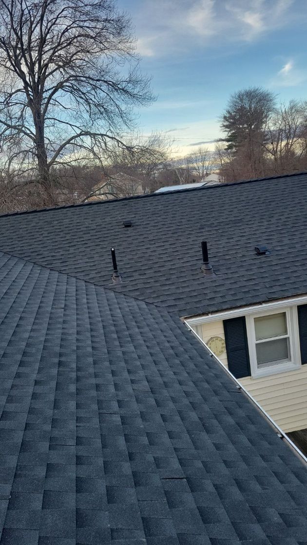 Dark gray shingle roof, vents, and a partially visible white building, with a blue sky background.