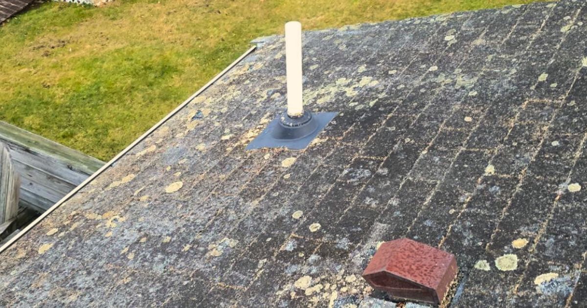 A weathered roof with a vent pipe and a brick on top.