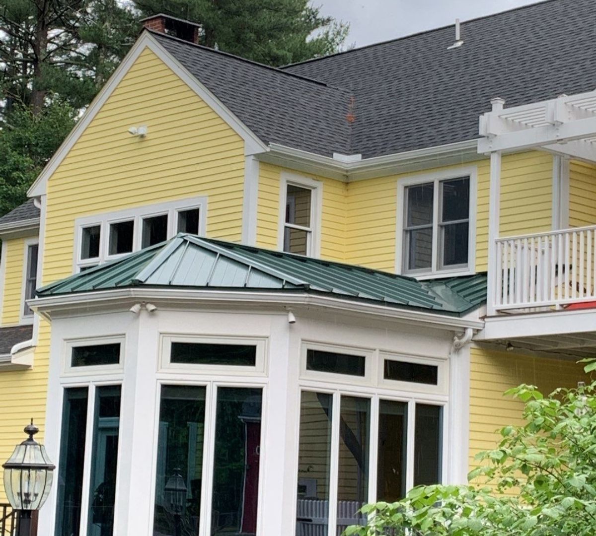 Yellow house with a green-roofed sunroom. White windows and trim. Dark roof.