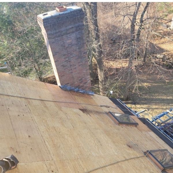 An unfinished wooden roof deck with a brick chimney and two skylights in a residential outdoor setting.