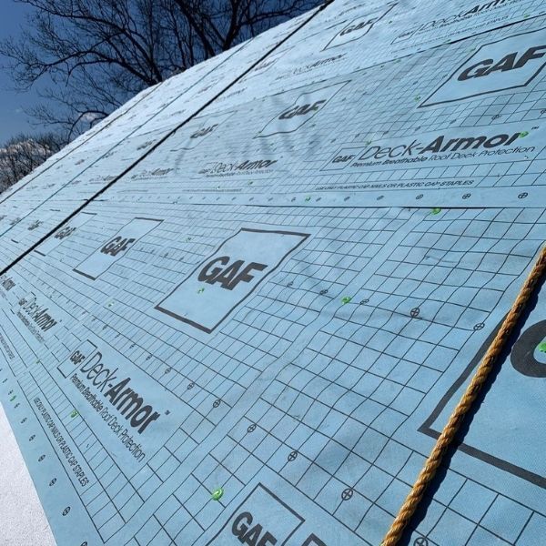 A sloped roof covered in blue GAF Deck-Armor underlayment featuring a grid pattern, with a safety rope running across it.