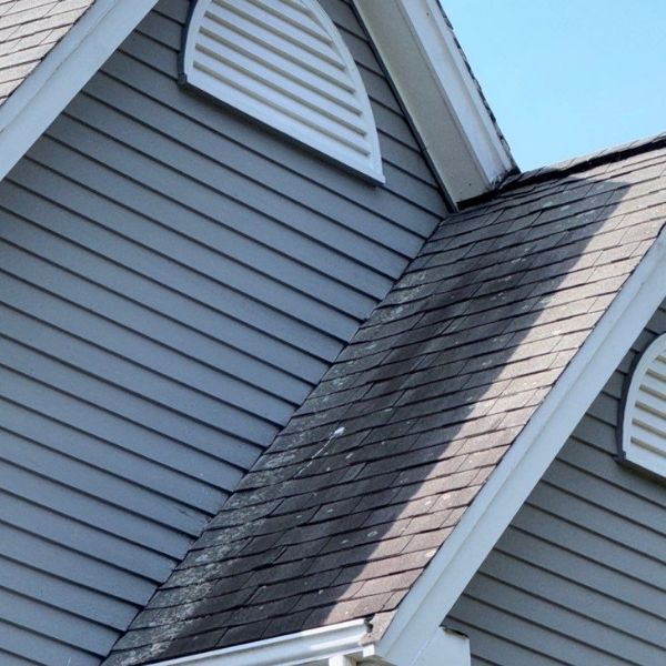 Gray siding and roof with dark streaks, triangular vents and white trim.