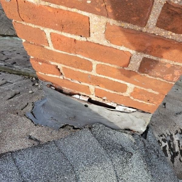 A damaged chimney flashing with a large gap between the roof flashing and the brickwork, showing signs of deterioration.