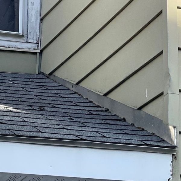 An exterior view of a house showing a roof meeting a wall with tan siding and metal flashing.