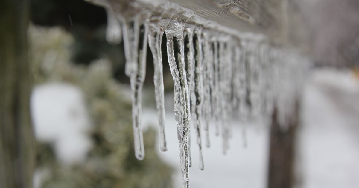 A close-up view of clear icicles hanging from a wooden surface during a snowy winter day.
