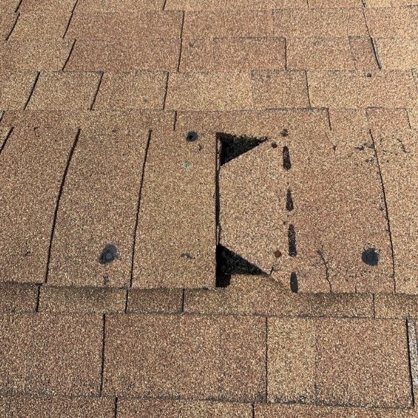 A damaged asphalt roof shingle with a missing triangular section, revealing the underlying layer.