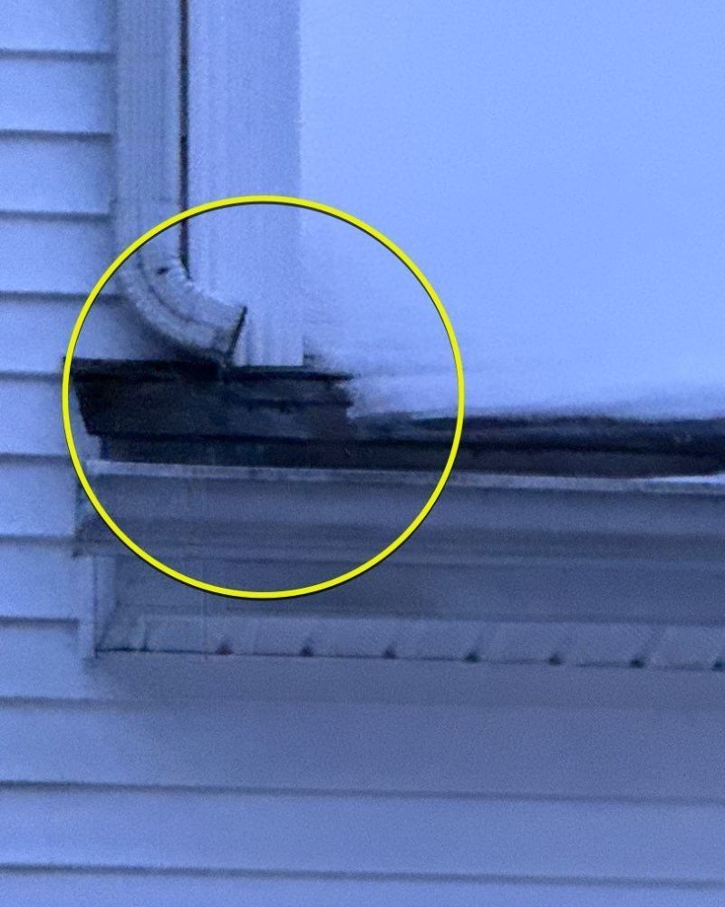 Gutter with snow buildup, near a white building's side, with siding and a downspout, in a cold weather setting.