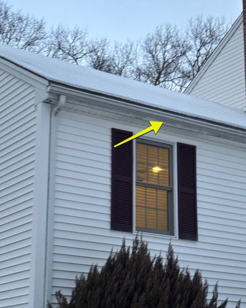 White house exterior with snow on roof, dark shutters, yellow arrow pointing to the roof.