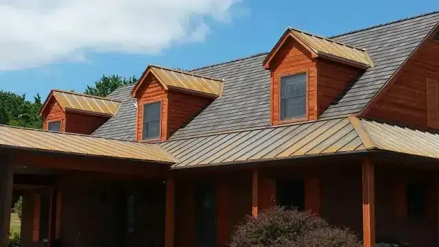 Brown house with dormers, weathered brown roof, and blue sky.
