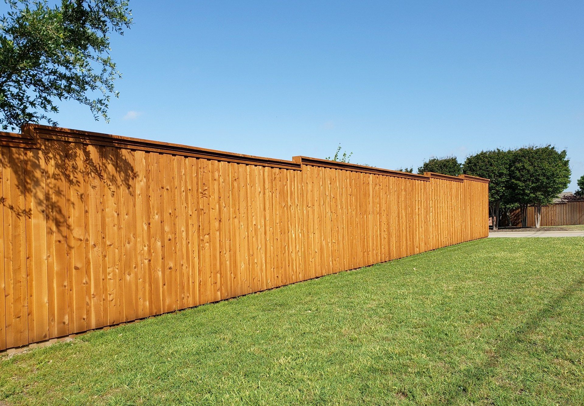 Long wooden privacy fence beside a green lawn under a clear blue sky
