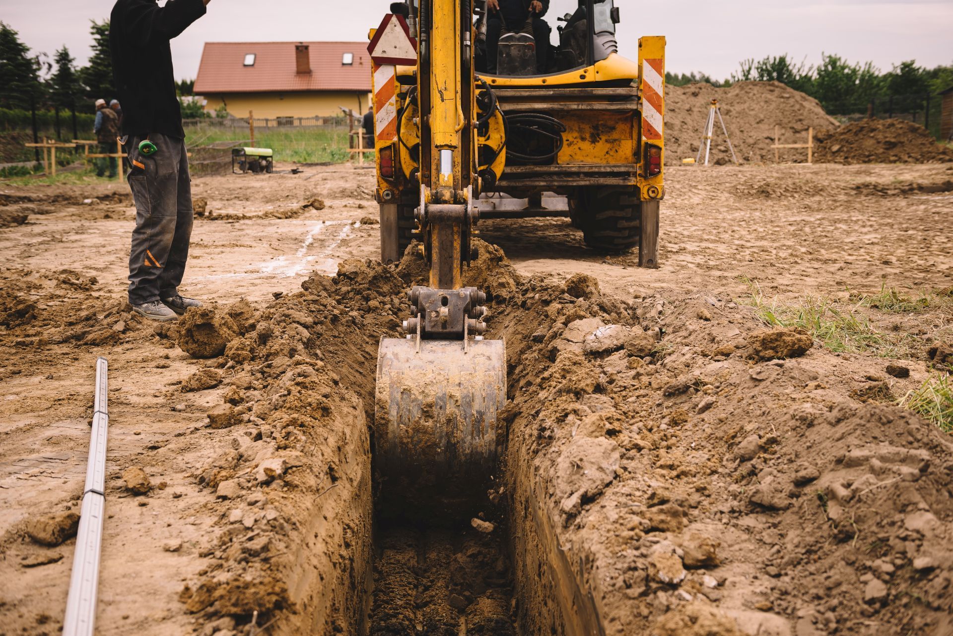 Excavator digging a trench at a muddy construction site with a worker nearby.