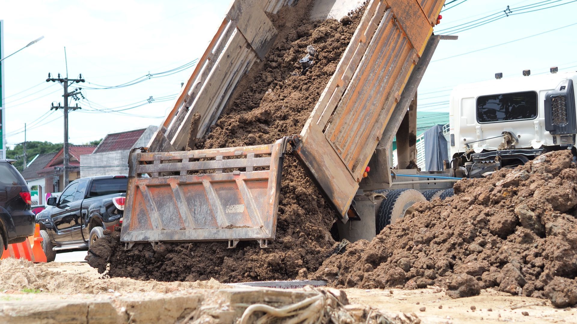 Dump truck unloading muddy soil at a construction site, with workers and another truck nearby.